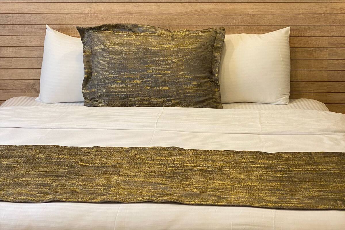 A bed with a wooden headboard, two white pillows, and a textured gold throw blanket.