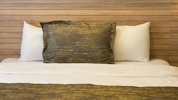 A bed with a wooden headboard, two white pillows, and a textured gold throw blanket.