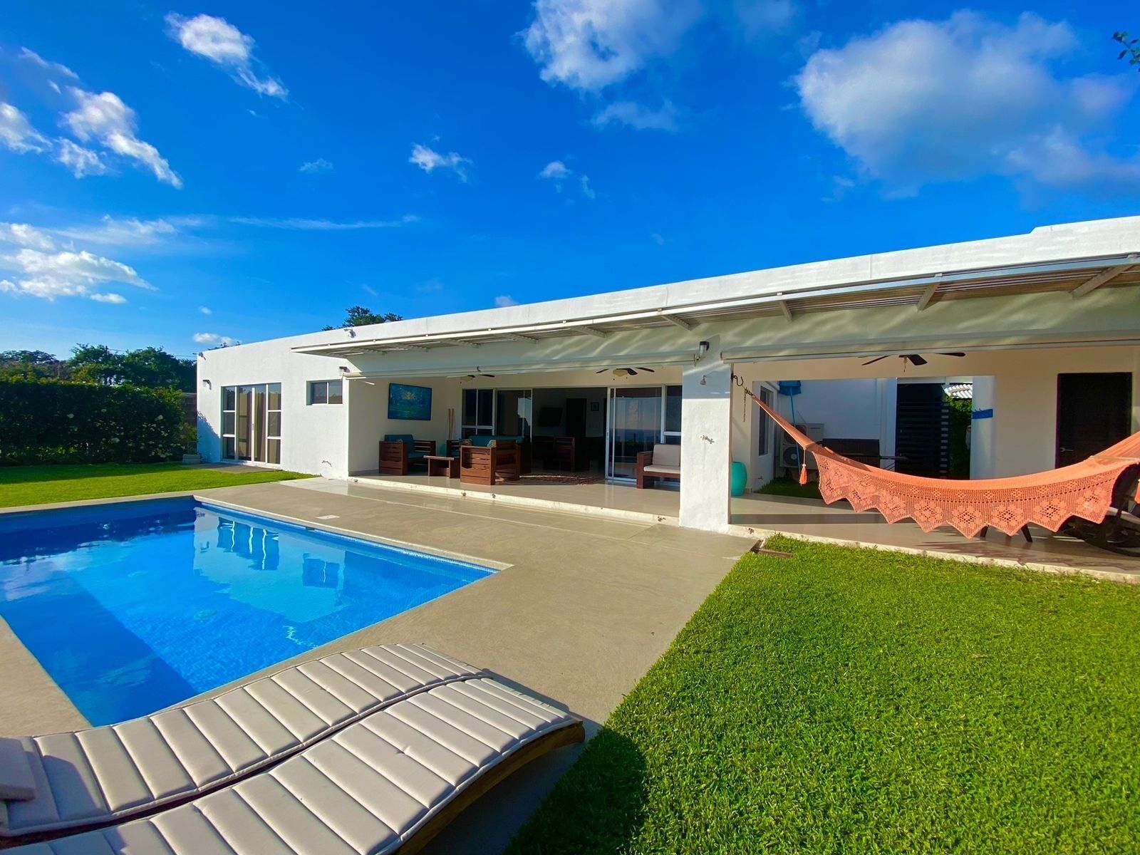 Una casa moderna con piscina, mobiliario exterior y una hamaca.