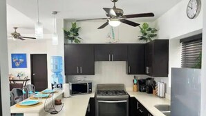 Une cuisine de taille réduite, dotée de meubles de rangement sombres, d’un four à micro-ondes, d’une cuisinière et d’un ventilateur de plafond.
