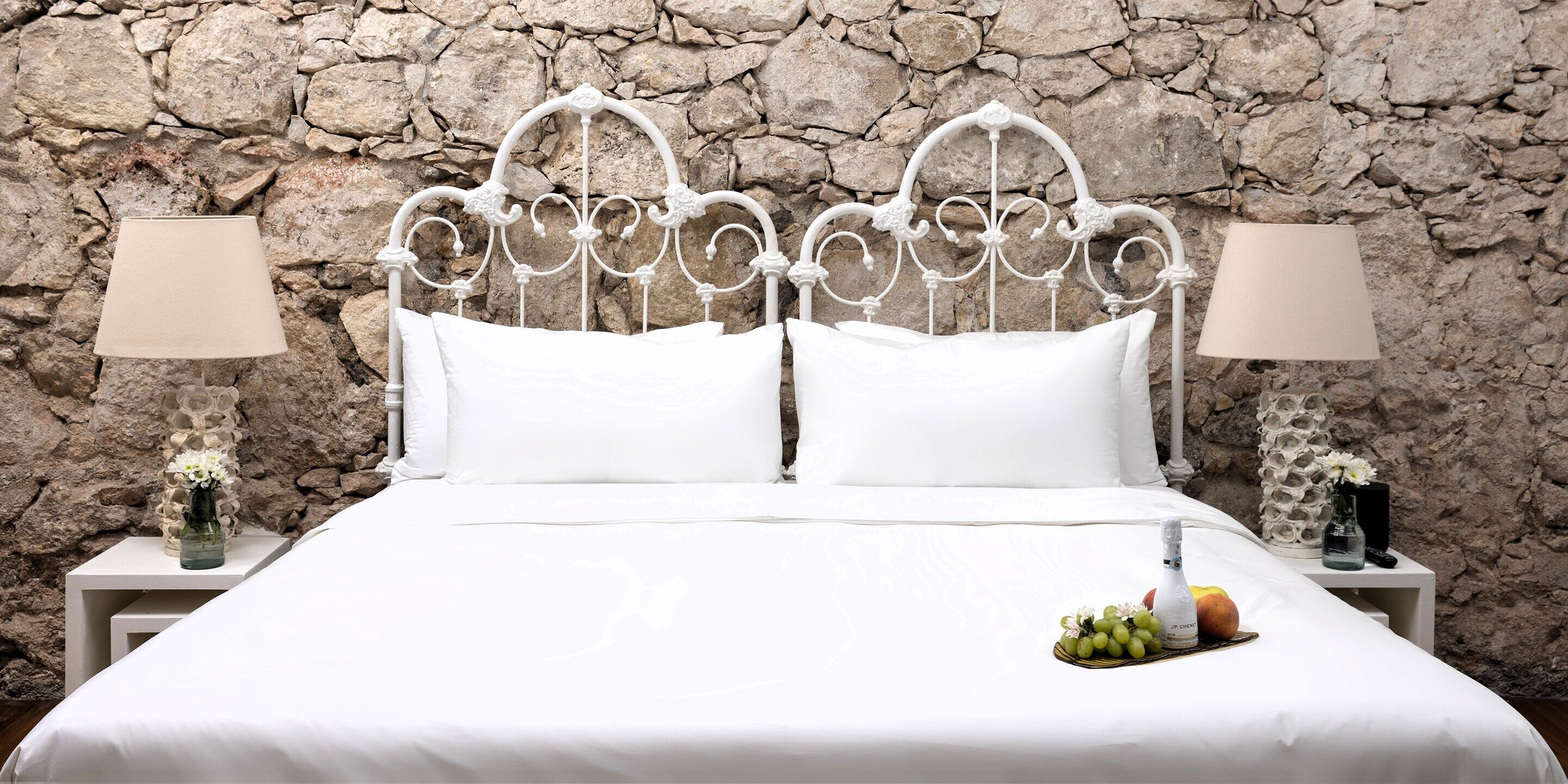 A bed with a white metal headboard, white bedding, and two bedside tables with lamps and vases.