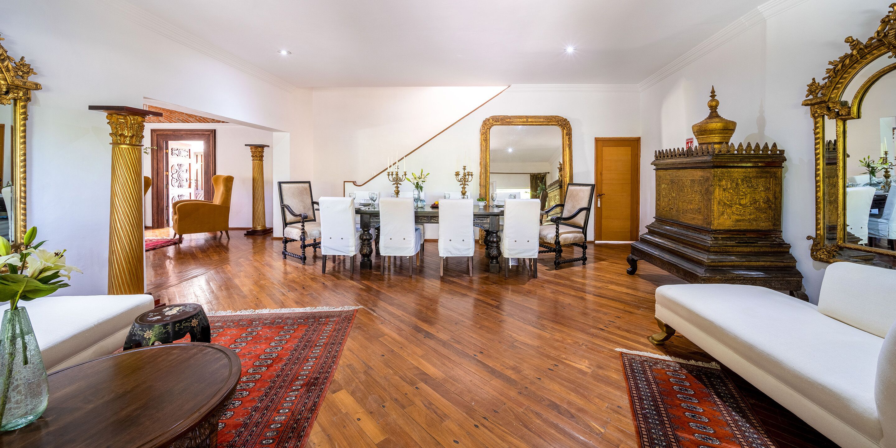 Un salón espacioso con piso de madera, un comedor con candelabro y un espejo grande y ornamentado.