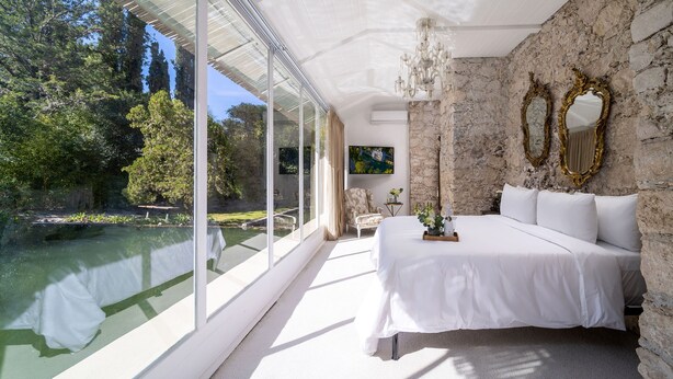 Ein Schlafzimmer mit einem großen Bett, Steinwänden und Blick auf einen Teich.