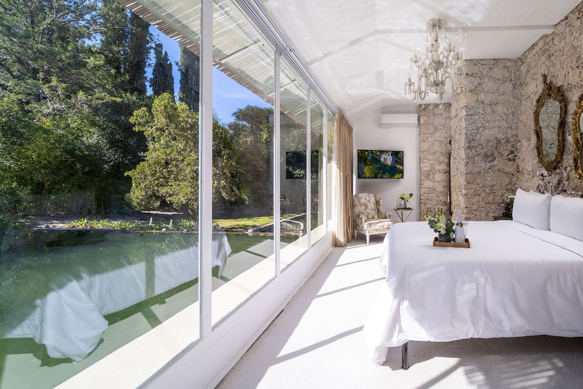 A bedroom with a large bed, stone walls, and a view of a pond.