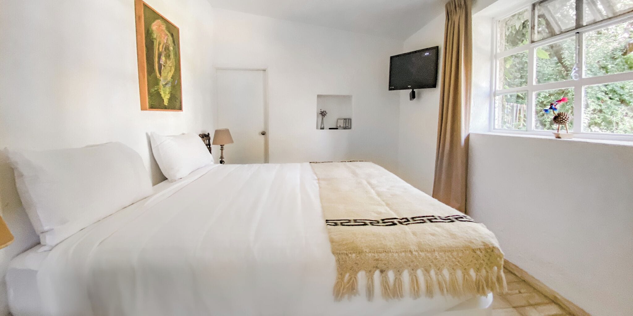 Un dormitorio con una cama, un televisor montado en la pared y un ventanal con cortinas.