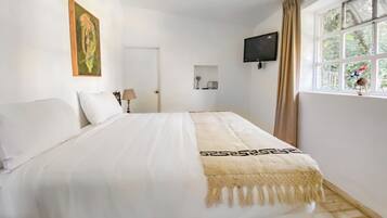 Un dormitorio con una cama, un televisor montado en la pared y un ventanal con cortinas.