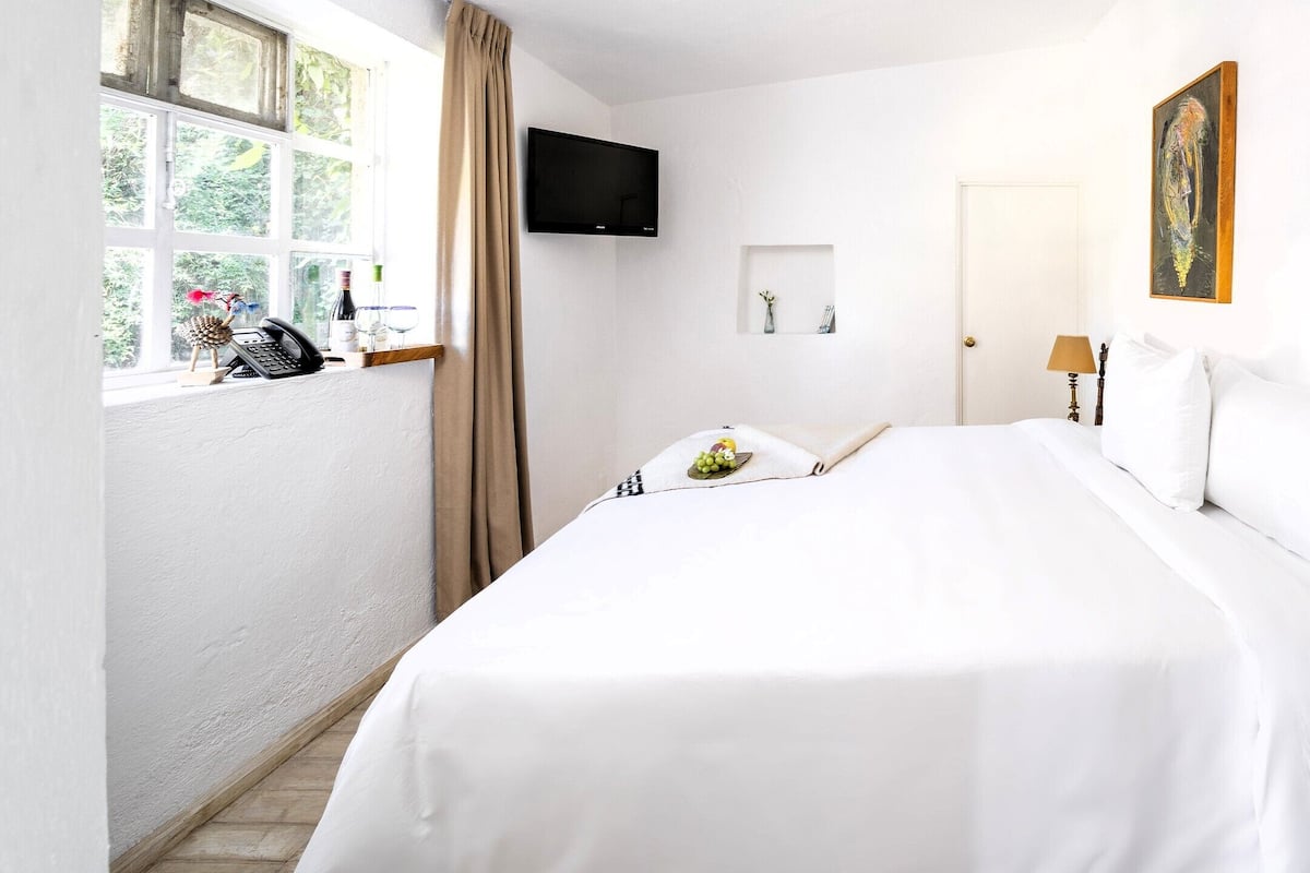 A hotel room with a large bed, a television mounted on the wall, a window with curtains, and a painting on the wall.