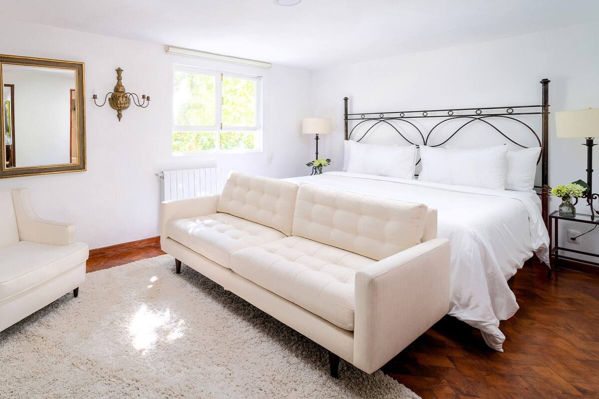 A bedroom with a bed, a white sofa, a mirror, and wall sconces.