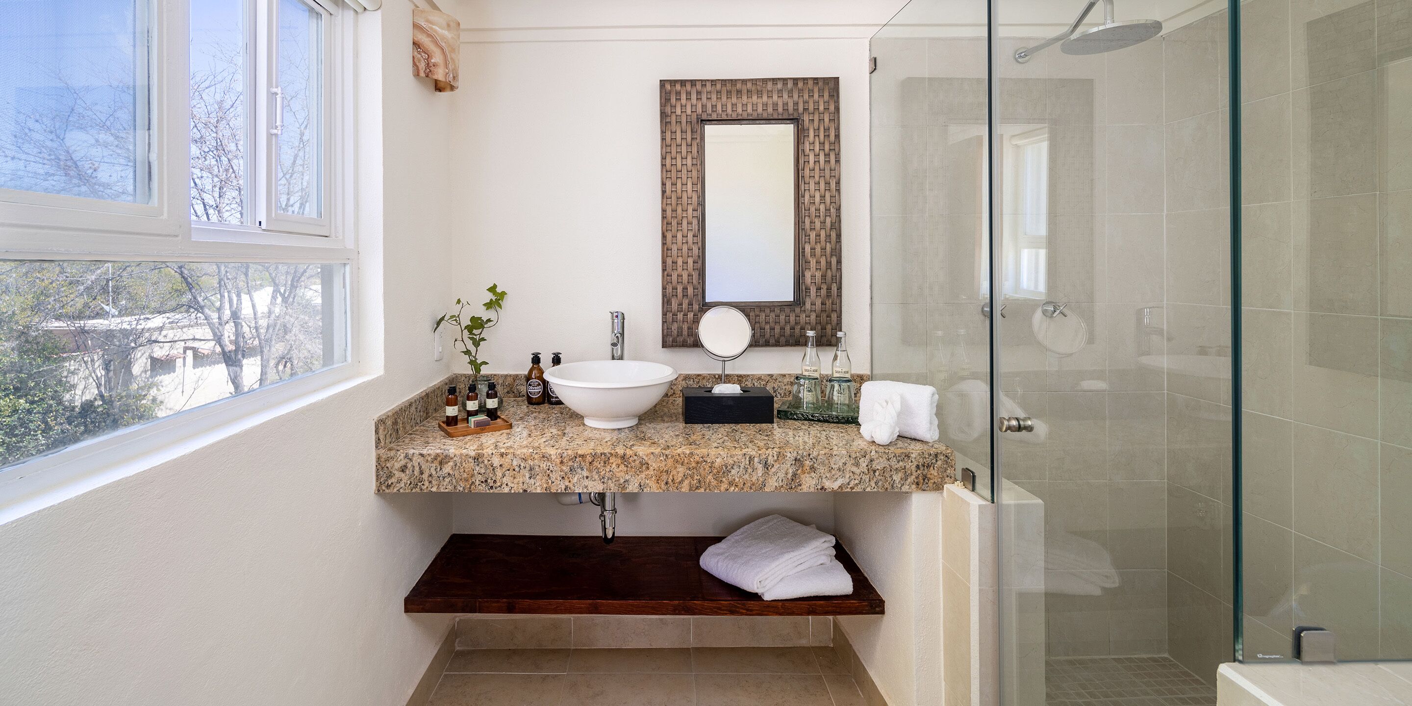A bathroom with a granite countertop, a white sink, a mirror, and a glass shower enclosure.