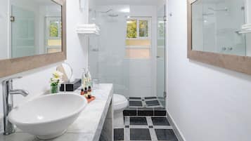 A modern bathroom with a large white sink, two mirrors, a glass shower enclosure, and a black and white tiled floor.
