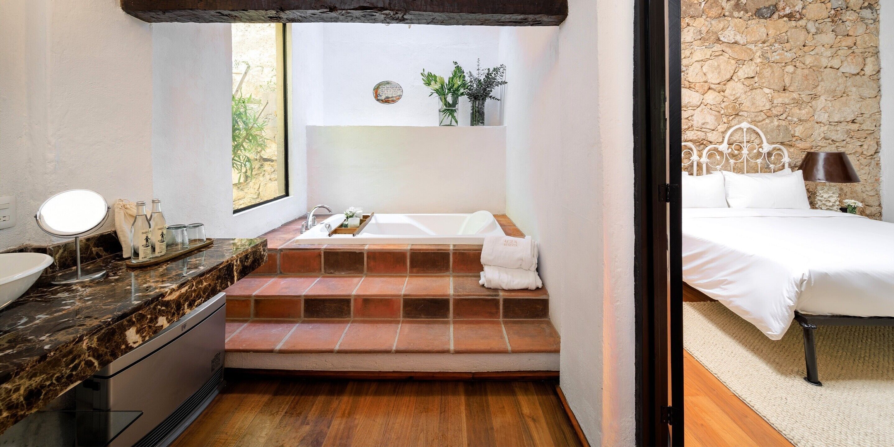 A bathroom with a marble countertop, a sink, a mirror, a bathtub, and a window with a view of greenery.