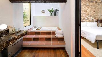 Un baño con encimera de mármol, lavabo, espejo, bañera y ventana con vistas a la vegetación.
