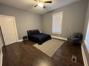 Une chambre à coucher comprenant un lit, une chaise, un ventilateur de plafond et une fenêtre avec des stores.