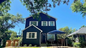 Een tweelaags huis met een donkerblauwe gevel, een voortuin met een blauwe parasol en een duidelijke voordeur.