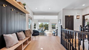 A spacious hallway with a wooden bench, a staircase with black balusters, and a view to a balcony with outdoor furniture.