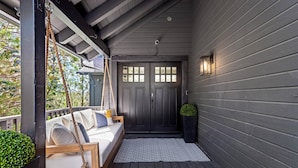 A porch with a swing seat, a dark wooden door, and a small potted plant.