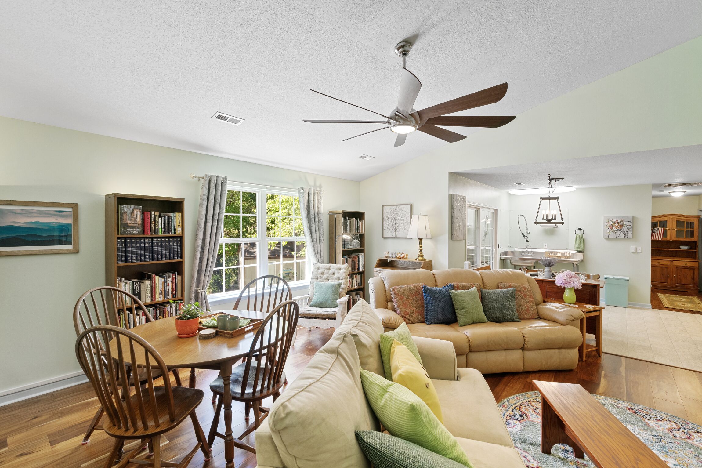 A spacious living room with a large sofa, a dining table, and a ceiling fan.