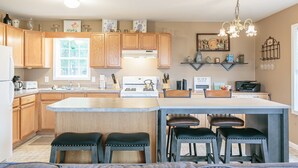 A modern kitchen with wooden cabinets, a central island with stools, a built-in oven, and a chandelier. - Welcome to the "Quay" Finger Lakes (Hammondsport)