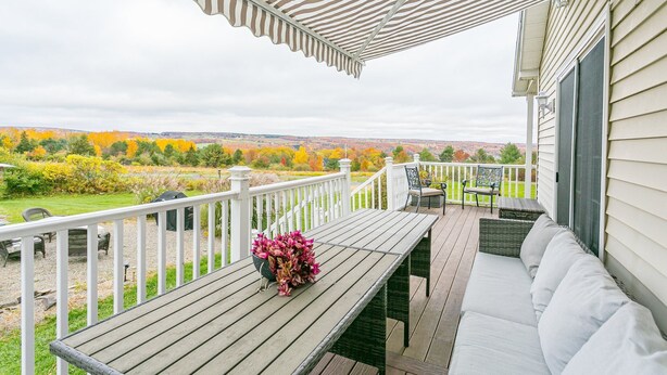 A covered outdoor deck with a wooden table and a bench, overlooking a landscaped garden with autumn foliage. - Welcome to the "Quay" Finger Lakes (Hammondsport)