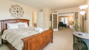 A bedroom with a wooden bed, a large decorative wall piece, and a hallway leading to a living area with a chair and a lamp. - Welcome to the "Quay" Finger Lakes (Hammondsport)
