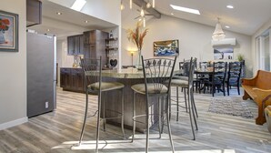Una cocina moderna con una isla central, taburetes de bar y un comedor con candelabro.