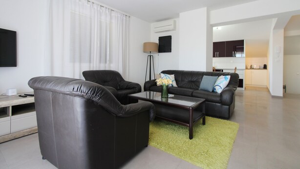 A modern living room with a sofa, armchair, and coffee table. There is a kitchen area visible in the background.