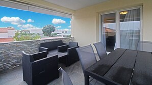 A balcony with wicker furniture, a table, and a view of buildings and trees.