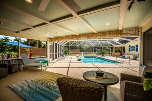 An outdoor patio with a pool, wicker furniture, and a covered area with a view of the backyard. - Tropical Getaway! Heated Pool, Tiki Bar, Pirate Sandbox, and Boat Parking! (Vero Beach)