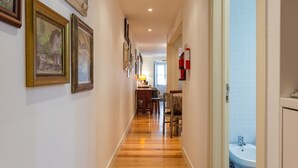 Un corridoio con pavimento in legno, quadri appesi alle pareti, una sala da pranzo con sedie e tavolo, e un bagno con lavandino e piastrelle.