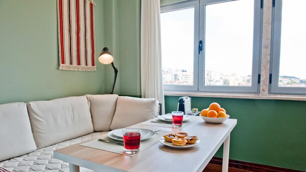 Una habitación acogedora con un sofá, una mesa con una bebida y pasteles, una lámpara y una ventana con vistas.
