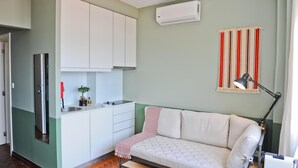 Un espacio habitable compacto con kitchenette, un sofá, una mesita y una lámpara.