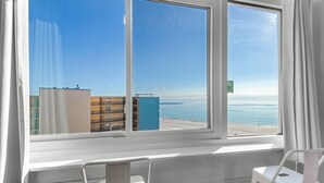 A room with a large window overlooking a beach and buildings. There are two white chairs in the foreground. - ☀️Gulf View- Updated- Pool- Studio Top of the Gulf 807☀️ (Panama City)