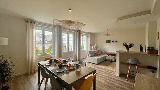 A modern living room with a dining area, large windows, and a kitchen area. - BLEU COMME MER - T2 apartment just a stone's throw from the beach (Concarneau)