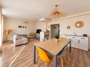 Una sala moderna con un sofá, una mesa de comedor con sillas, un televisor y una cocina con armarios.
