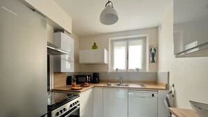 A modern kitchen with white cabinetry, a built-in oven, a microwave, and a sink. - BLEU COMME MER - T2 apartment just a stone's throw from the beach (Concarneau)