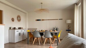 A modern living room with a grey sofa, a dining area with a table and chairs, a kitchen with cabinets and a radiator, and a decorative wall piece. - BLEU COMME MER - T2 apartment just a stone's throw from the beach (Concarneau)