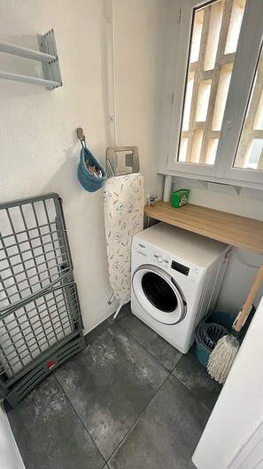 Ein kleiner Waschraum mit Waschmaschine, Wäscheständer, Besen und einem Fenster mit Blick.