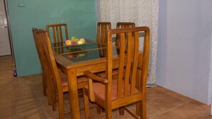 A dining table with six wooden chairs, a glass top, and a fruit centerpiece.