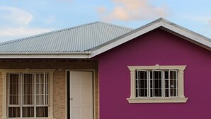 A single-story house with a purple exterior, a white door, and a window with a 'SOLD' sign.