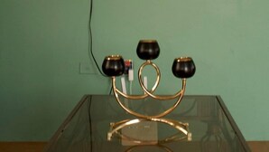 A room with a flat-screen TV mounted on a green wall, a glass table with a gold and black lamp, and a power cord.