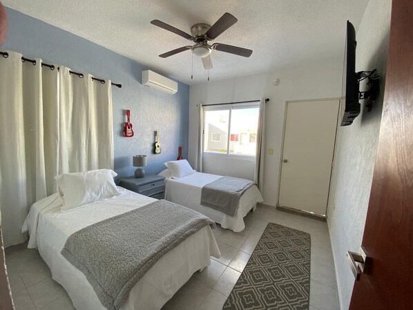 A hotel room with two beds, a ceiling fan, a guitar, and a window with curtains.