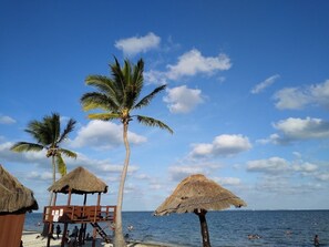 A beach with palm trees, thatched-roof structures, and people swimming in the water.