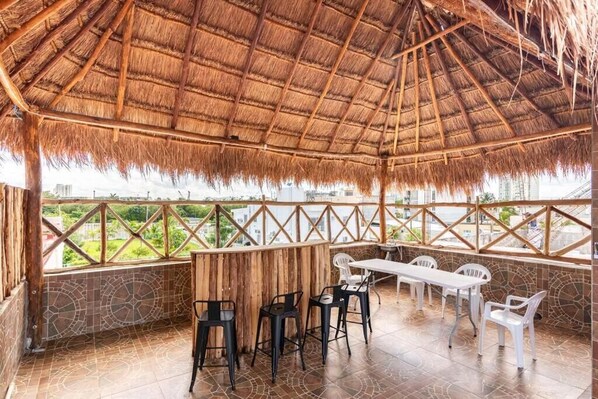 An outdoor patio with a thatched roof, stone walls, and a view of the cityscape.