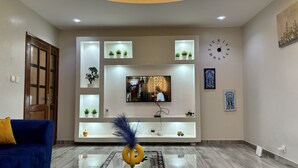 Een moderne woonkamer met een flatscreen televisie aan een wand, omringd door planken met potplanten.