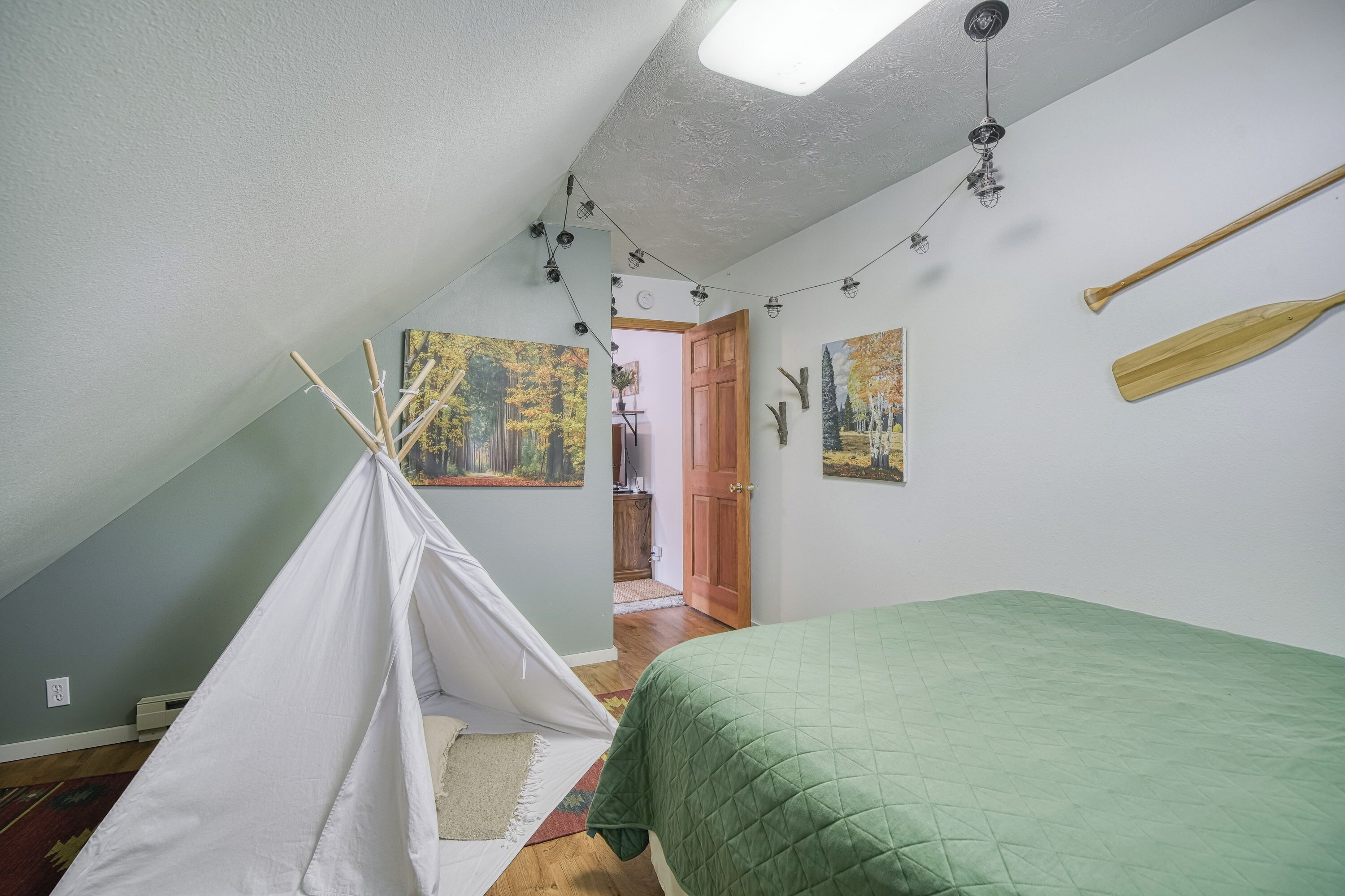 A bedroom with a green bed, a white tent, and paintings on the walls.