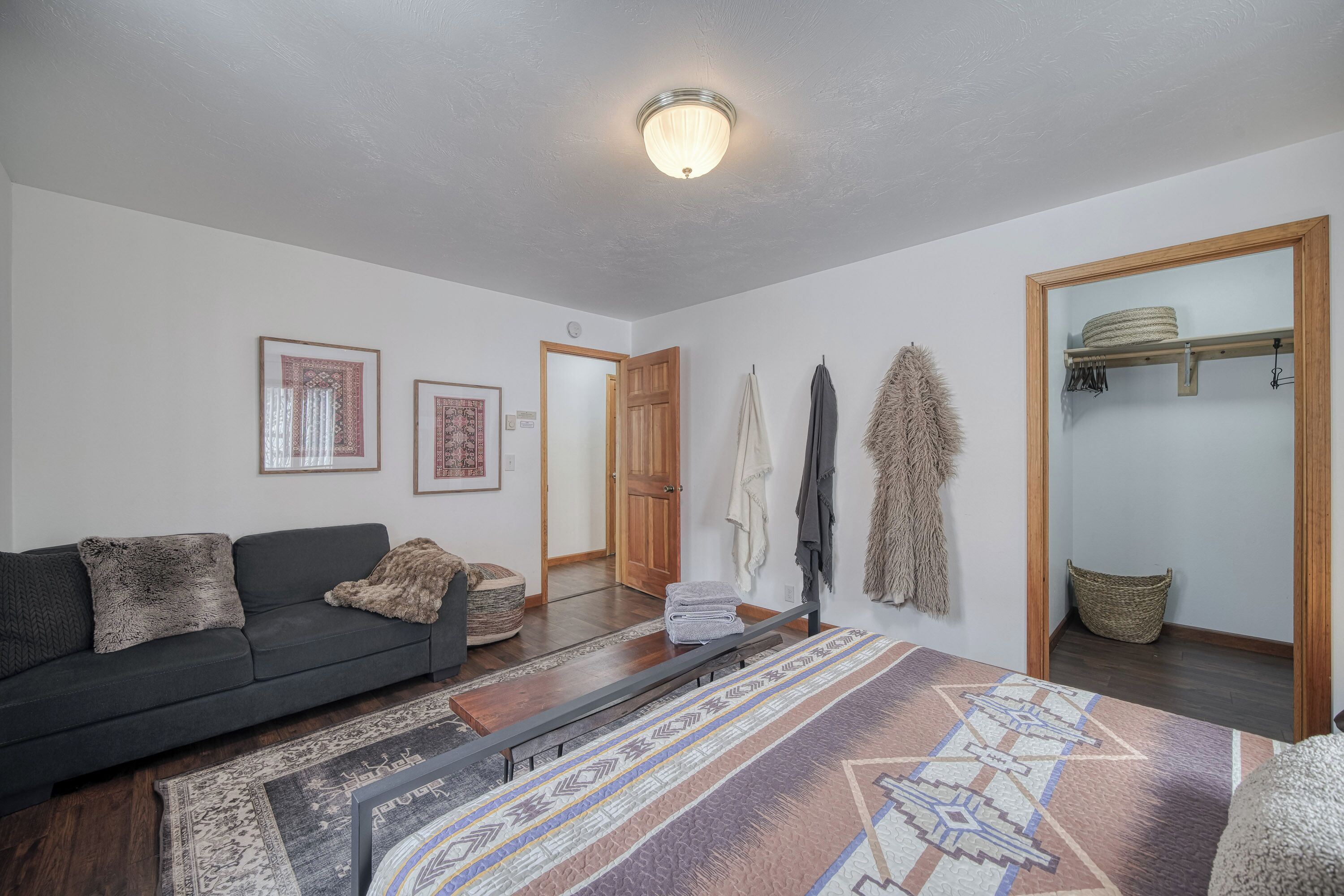 Una sala de estar con un sofá oscuro, un tapete estampado, un banco de madera y una puerta que da a otra habitación.