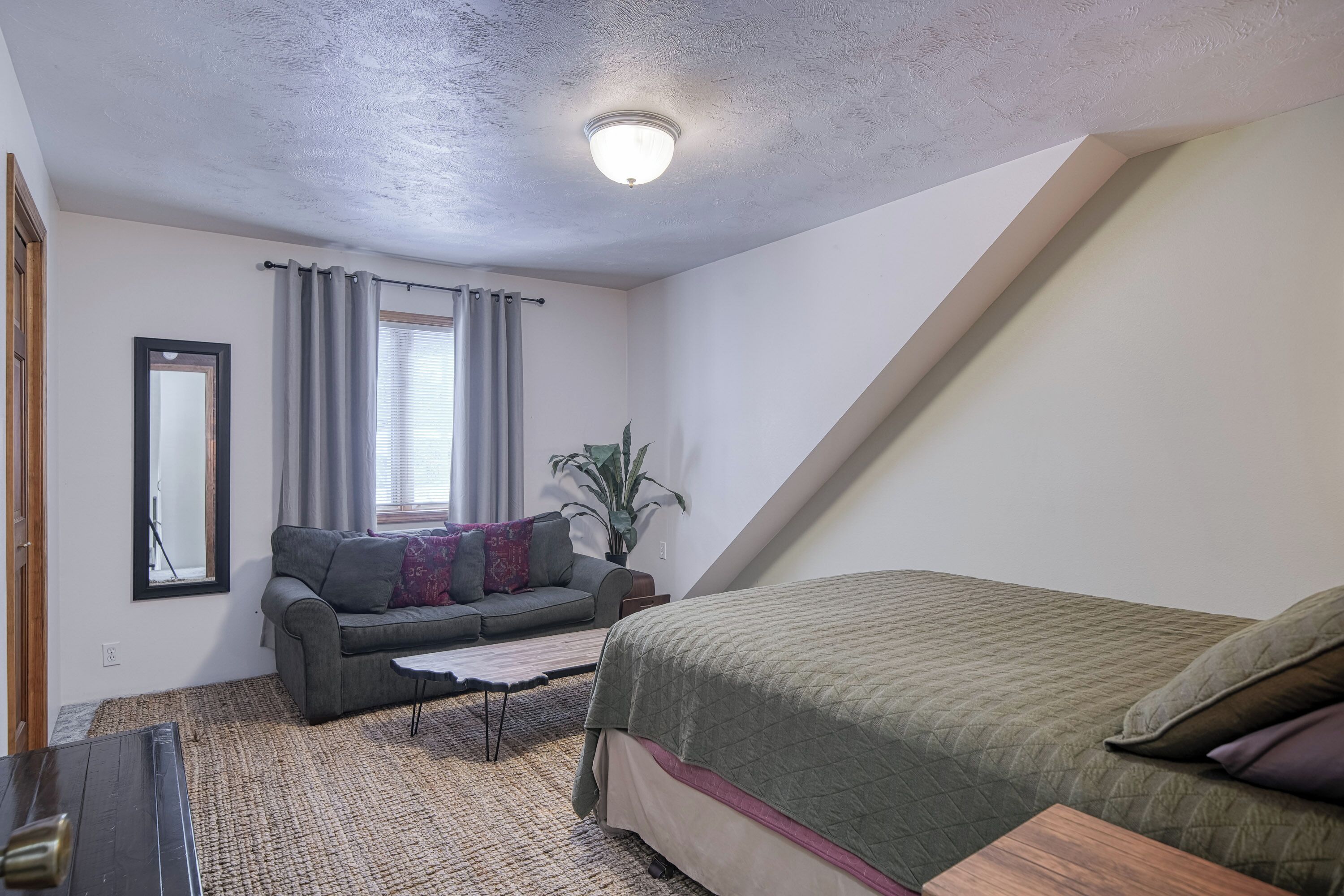 Een kleine, goed verlichte kamer met een bed, een bank, een bijzettafeltje en een plant.