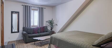 Een kleine, goed verlichte kamer met een bed, een bank, een bijzettafeltje en een plant.