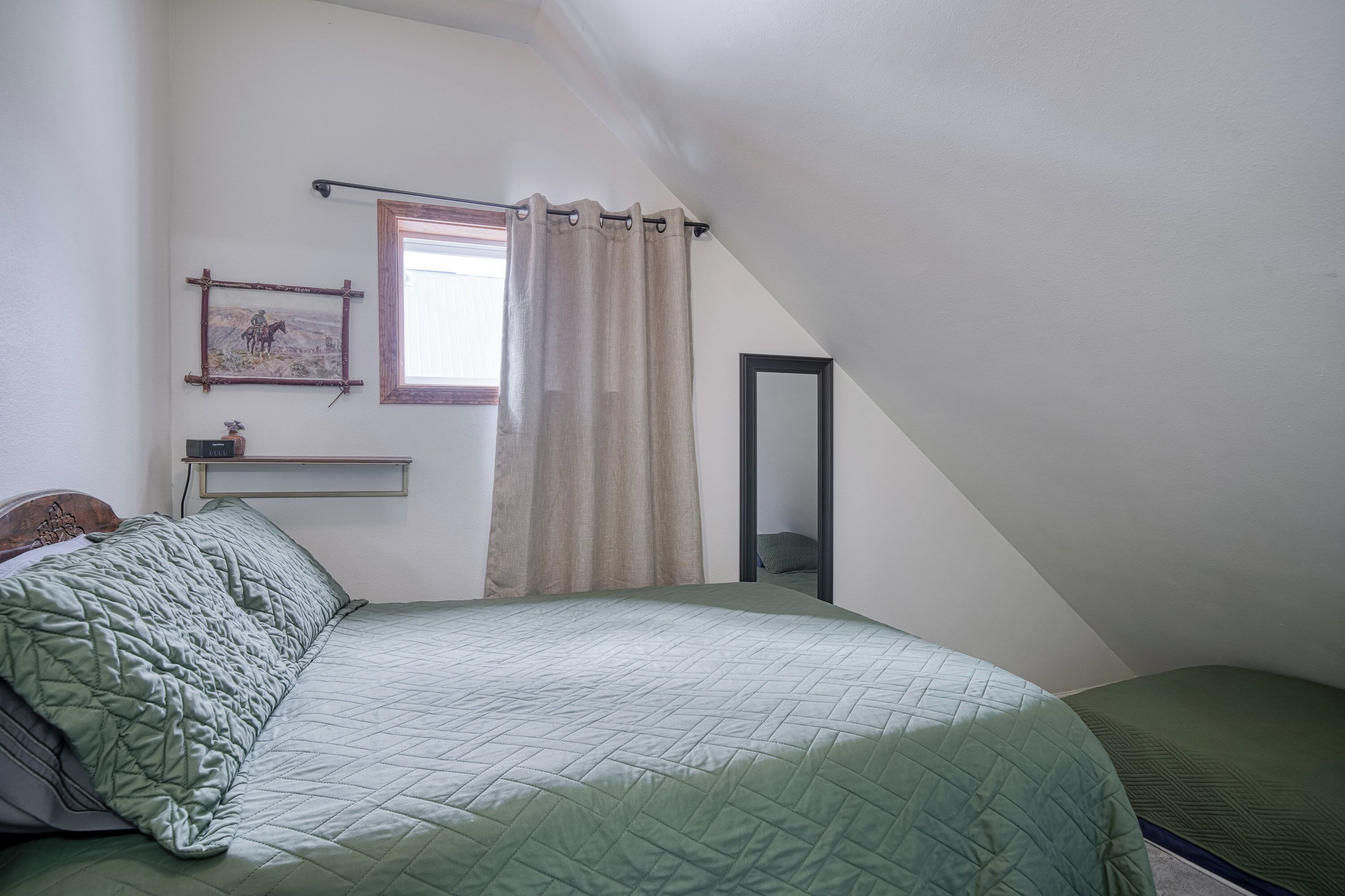 Un dormitorio con cama, una ventana con cortinas, una mesita de noche y un espejo.