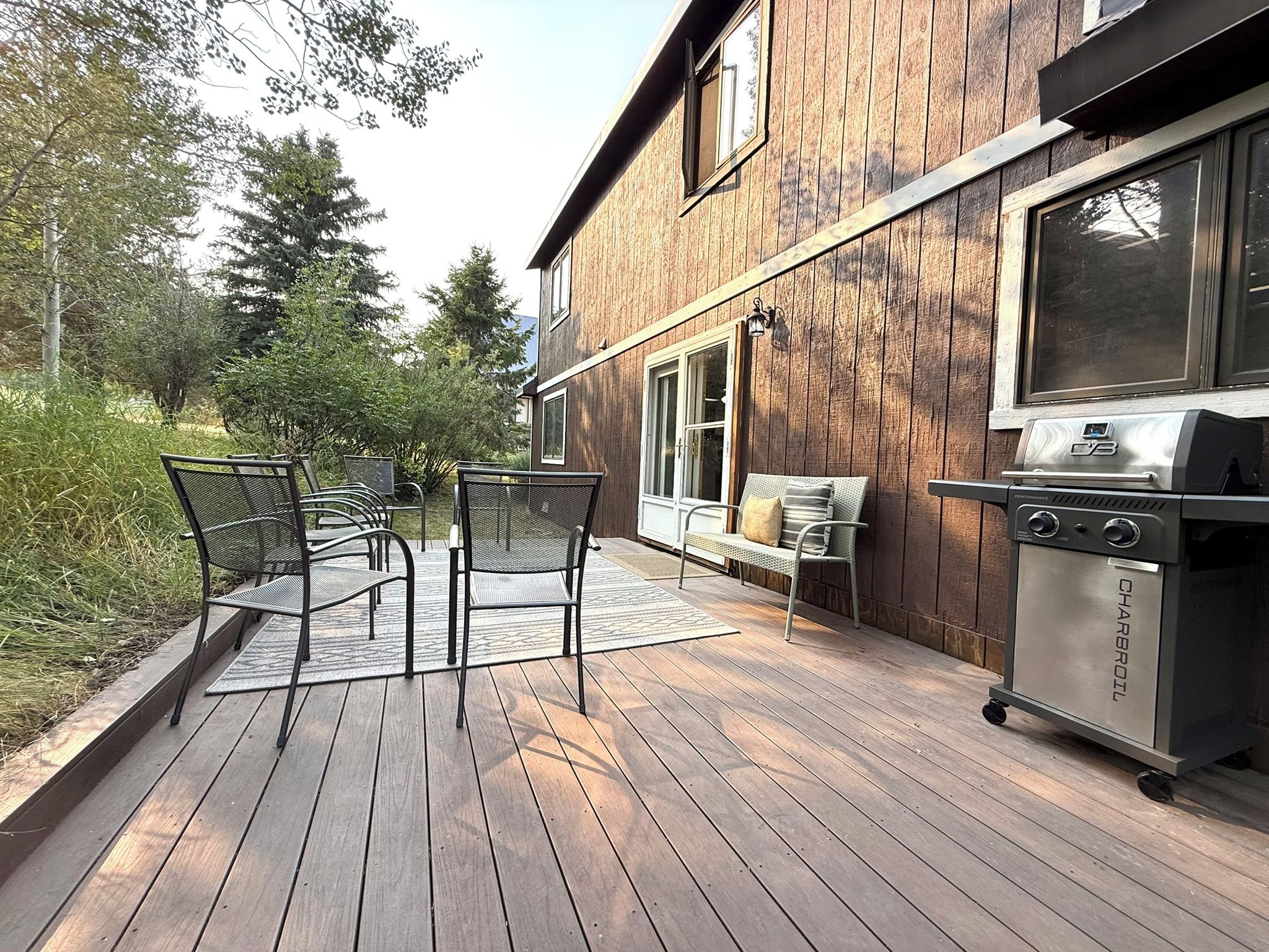 A wooden deck with outdoor furniture, a barbecue grill, and a house with a large window.